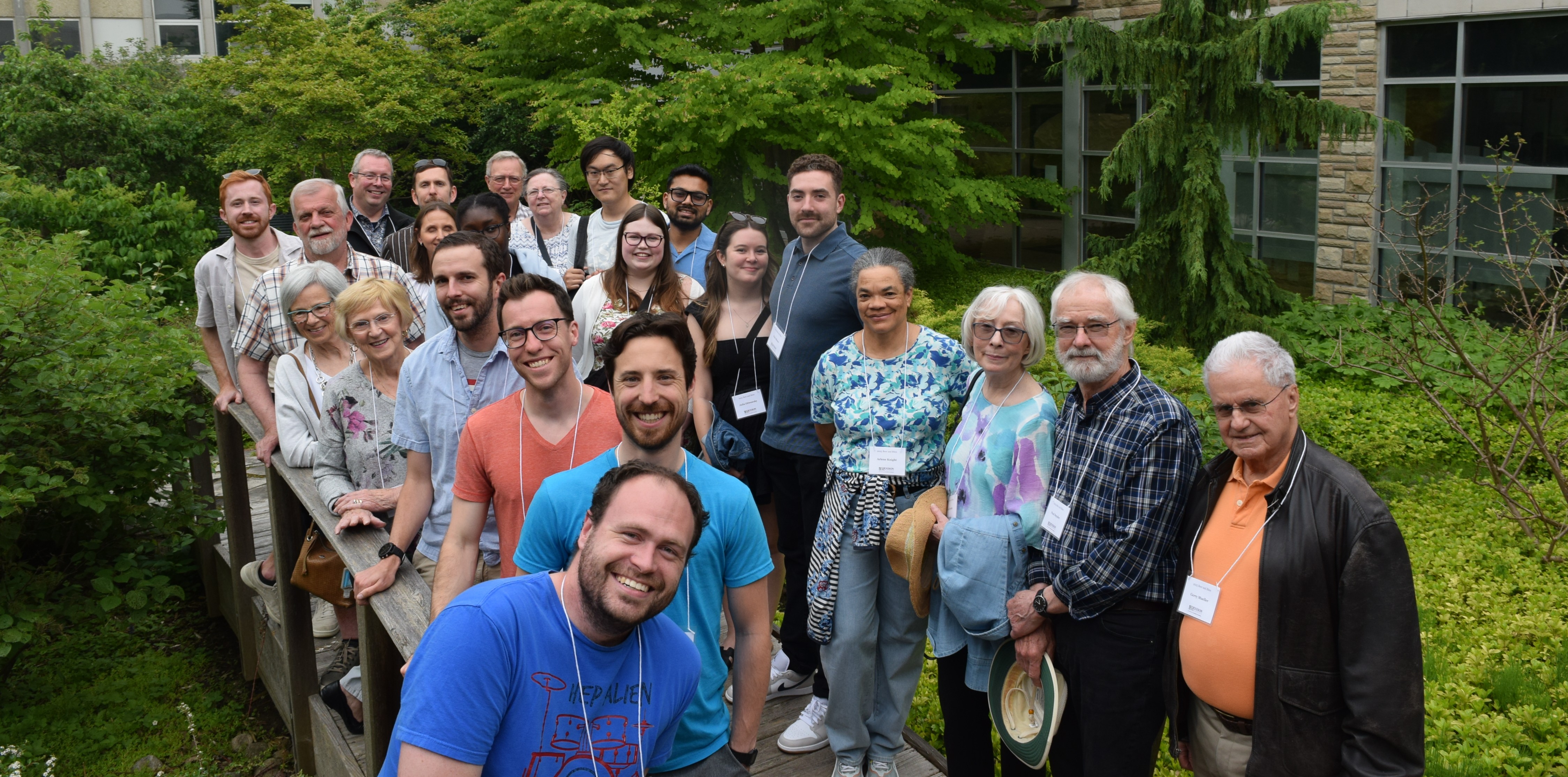 Group of alumni stand on the bridge in the Renison courtyard. Everyone is smiling and all are wearing name tags from the event.